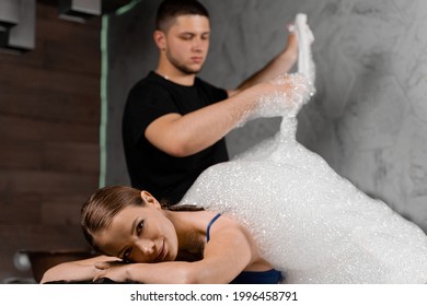 Attractive Girl Relaxing In Spa. Masseur Is Making Foam Peeling In Turkish Spa Hammam