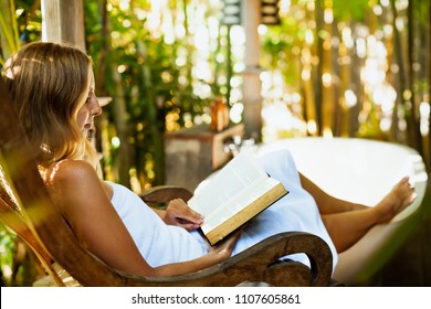 Attractive Girl Sit At Rocking Chair Drinking Morning Coffee, Reading Romance In Paper Book. Relaxing Woman Fill Bath Tub In Boho Style Outside Bathroom In Luxury Villa On Summer Tropical Vacation.