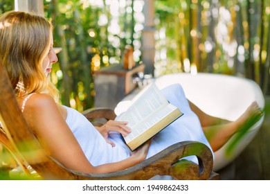 Attractive Girl Sit At Rocking Chair Drinking Morning Coffee, Reading Romance In Paper Book. Relaxing Woman Fill Bath Tub In Boho Style Outside Bathroom In Luxury Villa On Summer Tropical Vacation.