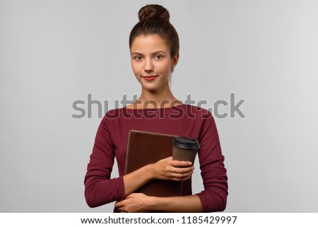 Attractive girl student holding a folder with educational supplies and a Cup of coffee. Tense and mixed emotions on her face. Studio portrait on isolated background. The concept of training.