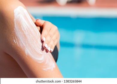Attractive girl in sunhat applying sunscreen on shoulder by the pool. Sun Protection Factor in vacation, concept.