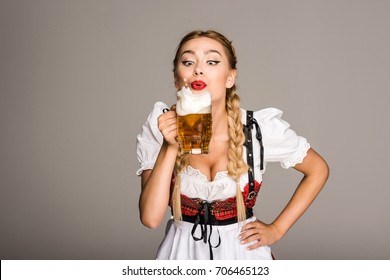 attractive girl in traditional german costume drinking beer on Oktoberfest, isolated on grey  