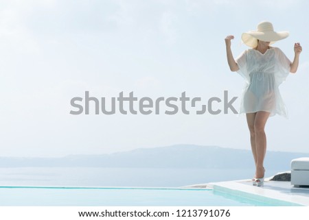 attractive girl in tunic and wide-brimmed hat posing near the pool.