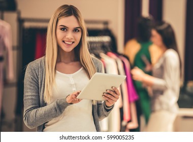 Attractive girl is using a digital tablet, looking at camera and smiling while doing shopping in the mall - Shutterstock ID 599005235