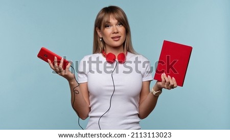 Attractive Girl Wearing in White Basic T-shirt and Red Headphones. Young Woman Holding Hands of Red Book and Mobile Phone. Read Textbooks or Listen Audiobooks. Choice is Yours. Knowledge is Power. Stock photo © 