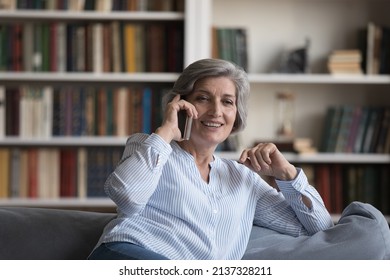 Attractive Grey-haired Middle-aged Woman Relaxing Alone At Home Sit On Sofa Holds Cell Phone Having Pleasant Conversation. Remote Communication, Making Call, Older Generation Using Modern Tech Concept