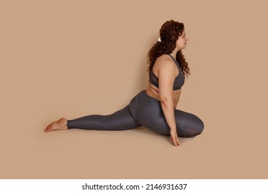 Attractive groomed fat obese plump woman doing sports stretch, sitting half splits. Exercises for spine and muscles. Burning fast calories, self acceptance concept. Wearing gray sportswear. Copy space