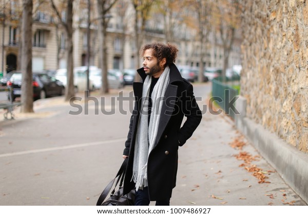 Attractive guy leaving city and going\
to railway station. Handsome man in black coat looks attractive.\
Concept of walking, hurrying and autumn\
depression.