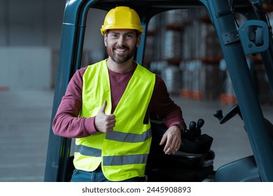 Attractive, handsome, bearded man, driver showing thumbs up, wearing helmet, standing near forklift, looking at camera, standing in warehouse. Concept of logistics, vehicle - Powered by Shutterstock