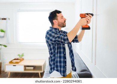 Atractivo hombre a mano usando un taladro para poner fotos y decoraciones en la pared después de mudarse a una casa nueva