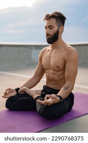 attractive hansome man with athletic strong body doing morning yoga asana outdoors and having dzen meditation