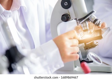 Attraktiver Glückswissenschaftler oder Arzt, der Mikroskop-Testproben im Labor mit Glaswaren im Labor verwendet. Wissenschaftliche oder medizinische Forschung und Entwicklung neuer antiviraler oder Covid-19-Impfstoff-Konzept.