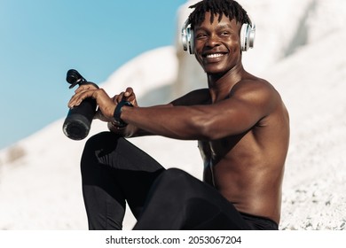 Attractive happy african american fitness man listening to music in headphones sitting outdoors relaxing after workout using smartwatch - Powered by Shutterstock