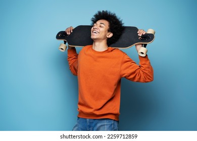 Attractive happy African American man with closed eyes holding longboard isolated on blue background. Active lifestyle concept