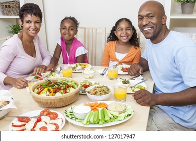 An Attractive Happy African American, Smiling Family Of Mother, Father, Two Daughters Eating Salad And Healthy Food At A Dining Table.