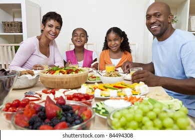 An Attractive Happy African American, Smiling Family Of Mother, Father, Two Daughters Eating Salad And Healthy Food At A Dining Table.