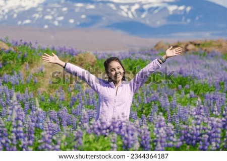 Attractive happy asian woman standing and smiling in lupine flower blooming field on summer at Iceland