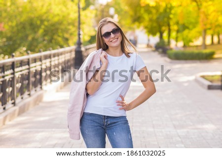 Attractive happy blonde Caucasian young woman wearing casual clothes and sunglasses walking in a park on a warm spring day. Style, fashion, lifestyle.