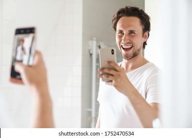 Attractive Happy Confident Young Man Standing In Front Of The Bathroom Mirror, Taking A Selfie