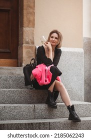 Attractive Happy Girl In A Black Dress In A City Street With A Glass Of Wine. Glamorous Lifestyle. Fashion.