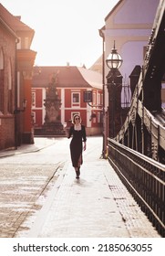 Attractive Happy Girl In A Black Dress  Walks Along A City Street With A Glass Of Wine. Glamorous Lifestyle. Fashion.