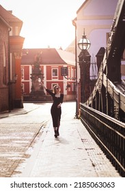 Attractive Happy Girl In A Black Dress  Walks Along A City Street With A Glass Of Wine. Glamorous Lifestyle. Fashion.