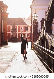 Attractive Happy Girl In A Black Dress  Walks Along A City Street With A Glass Of Wine. Glamorous Lifestyle. Fashion.