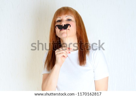Attractive happy middle aged woman having fun with a fake moustache on stick. Senior  female in period menopause. Lifestyle, Women's Health concept : playful  mature ready for party. Impostor syndrome