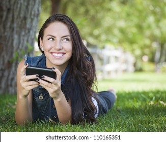 Attractive Happy Mixed Race Young Female Texting On Her Cell Phone Outside Laying In The Grass.