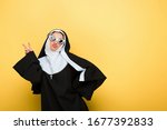 attractive happy nun in sunglasses showing victory sign on yellow