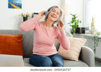 Attractive happy senior woman listening music in wireless headphones, having fun sitting on comfortable sofa at home. Technology, positive lifestyle concept  - Powered by Shutterstock