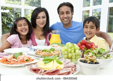 An Attractive Happy, Smiling Asian Indian Family Of Mother, Father, Son And Daughter Eating Healthy Food & Salad At A Dining Table.