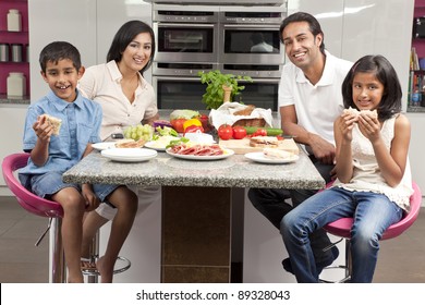 An Attractive Happy, Smiling Asian Indian Family Of Mother, Father, Son And Daughter Eating Healthy Food & Salad In The Kitchen At Home