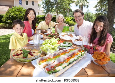 An Attractive Happy, Smiling Family Of Mother, Father, Grandparents, Son And Daughter Eating Healthy Food At A Picnic Table Outside