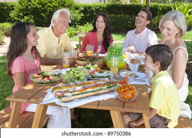 An Attractive Happy, Smiling Family Of Mother, Father, Grandparents, Son And Daughter Eating Healthy Food At A Picnic Table Outside