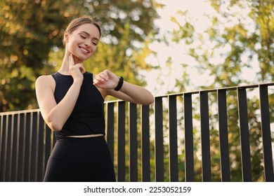Attractive happy woman checking pulse after training in park. Space for text - Shutterstock ID 2253052159