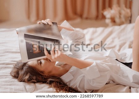 an attractive and happy woman lies in bed and reads a magazine. the concept of a happy weekend and rest at home.