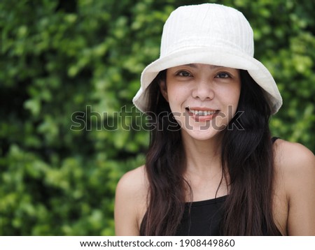 Attractive happy woman with long hair near lush green tree leaves on blurred background. Nature beauty concept