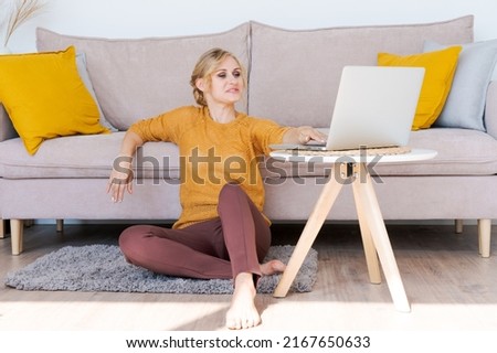 Attractive happy woman sitting on floor in living room smiling and looking at camera while working on laptop in home office. Young startup entrepreneur or freelance business concept.