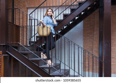 Attractive happy young asian woman going shopping walking down the stairs of a shopping plaza while talking to her smart phone