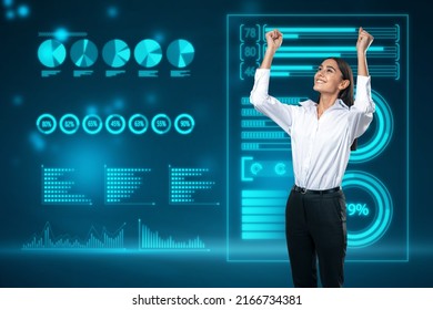 Attractive Happy Young European Businesswoman Celebrating Success On Abstract Glowing Background With Blue Business Charts And Graphs Hologram. Finance, Ai, Digital Transformation And Fintech Concept