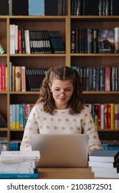 Attractive Happy Young Girl Student Studying At The College Library, Sitting At The Desk, Using Laptop Computer, Having Video Chat