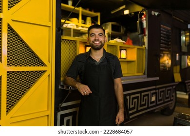 Attractive happy young man working during the night preparing street fast food at the food truck - Powered by Shutterstock