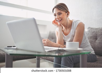 Attractive Happy Young Student Studying Online At Home, Using Laptop Computer, Headphones, Having Video Chat, Waving. Video Conference Or Virtual Event On Quarantine