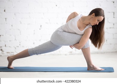 Attractive happy young woman working out indoors. Portrait of beautiful model doing exercises on blue mat in room with white walls. Revolved Side Angle Pose, Parivrtta Parsvakonasana. Full length - Powered by Shutterstock