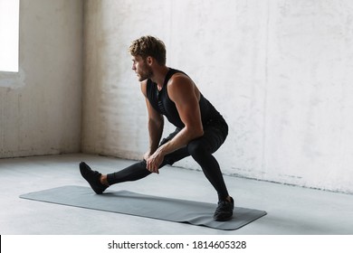 Attractive Healthy Uong Sports Man Stretching On Fitness Mat Indoors, Over Gray Wall Background