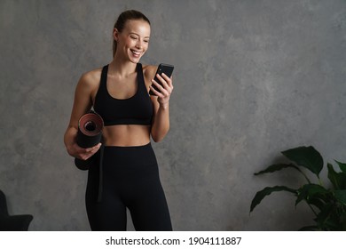 Attractive Healthy Young Woman With A Fitness Mat Using Mobile Phone At The Yoga Studio