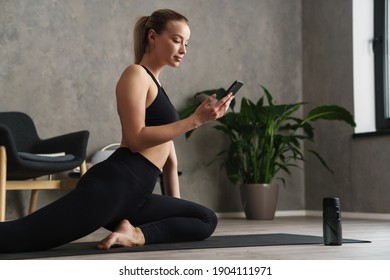 Attractive Healthy Young Woman With A Fitness Mat Using Mobile Phone At The Yoga Studio, Exercising