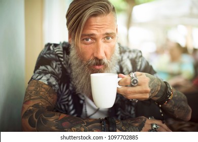 Attractive hipster with a beard is drinking coffee in a coffee shop 