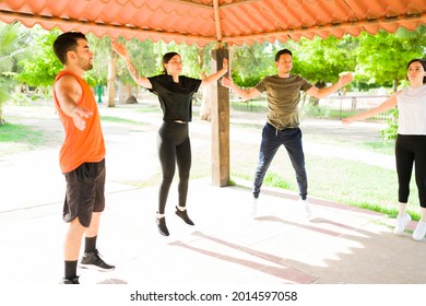 Attractive hispanic and caucasian young friends doing jumping jacks while exercising with a cardio workout outdoors - Powered by Shutterstock